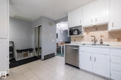 Kitchen featuring white cabinets, stainless steel dishwasher, light countertops, a chandelier, and tasteful backsplash - 