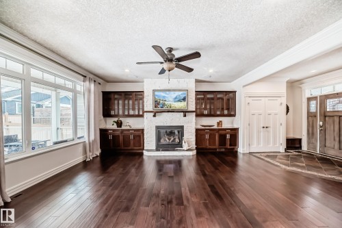 Unfurnished living room with dark wood-style flooring, crown molding, a ceiling fan, a fireplace, and a textured ceiling - 6 Wade Avenue, Leduc, AB - Indoor Photo Showing Living Room With Fireplace