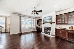 Unfurnished living room with a ceiling fan, dark wood-type flooring, a stone fireplace, a textured ceiling, and ornamental molding - 