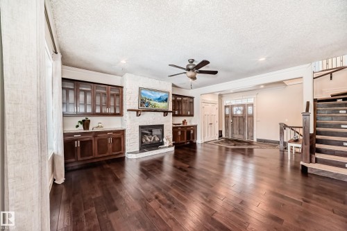 Unfurnished living room with stairway, dark wood-style floors, a textured ceiling, a fireplace, and ceiling fan - 6 Wade Avenue, Leduc, AB - Indoor Photo Showing Other Room With Fireplace