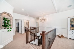 Hallway featuring an upstairs landing, light carpet, a chandelier, ornamental molding, and wainscoting - 