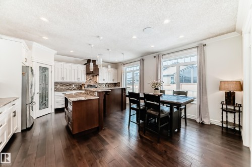 Kitchen featuring dark brown cabinets, white cabinetry, a center island with sink, crown molding, and light stone countertops - 6 Wade Avenue, Leduc, AB - Indoor