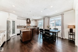 Kitchen featuring dark brown cabinets, white cabinetry, a center island with sink, crown molding, and light stone countertops - 
