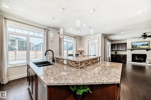 Kitchen featuring light stone countertops, an island with sink, hanging light fixtures, dark wood finished floors, and a textured ceiling - 6 Wade Avenue, Leduc, AB - Indoor Photo Showing Kitchen With Fireplace With Double Sink With Upgraded Kitchen