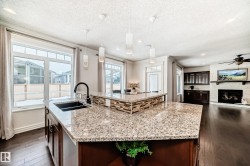 Kitchen featuring light stone countertops, an island with sink, hanging light fixtures, dark wood finished floors, and a textured ceiling - 