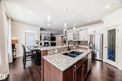 Kitchen featuring glass insert cabinets, pendant lighting, appliances with stainless steel finishes, dark wood finished floors, and a ceiling fan - 