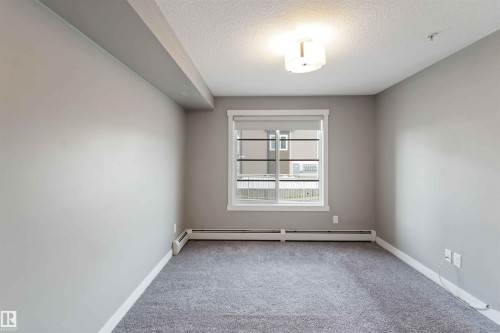 Spare room with a textured ceiling, light carpet, and baseboard heating - 101 3670 139 Avenue, Edmonton, AB - Indoor Photo Showing Other Room
