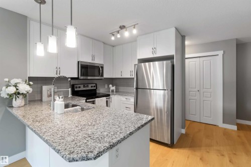 Kitchen with appliances with stainless steel finishes, decorative light fixtures, light stone counters, white cabinetry, and light wood-type flooring - 101 3670 139 Avenue, Edmonton, AB - Indoor Photo Showing Kitchen With Upgraded Kitchen