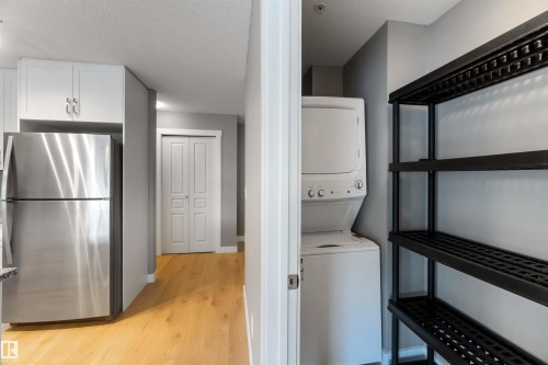 Laundry area featuring a textured ceiling, light wood finished floors, and stacked washing machine and dryer - 101 3670 139 Avenue, Edmonton, AB - Indoor Photo Showing Laundry Room