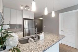 Kitchen with light stone counters, a peninsula, white cabinetry, stainless steel appliances, and hanging light fixtures - 