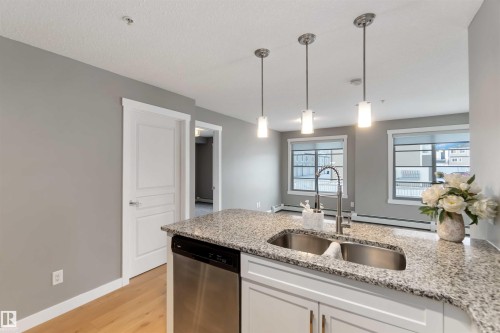 Kitchen with dishwasher, pendant lighting, light stone counters, light wood-style flooring, and a peninsula - 101 3670 139 Avenue, Edmonton, AB - Indoor Photo Showing Kitchen With Double Sink