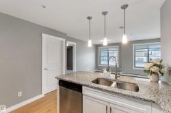 Kitchen with dishwasher, pendant lighting, light stone counters, light wood-style flooring, and a peninsula - 