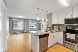 Kitchen featuring stainless steel appliances, white cabinetry, light stone counters, backsplash, and light wood-style floors - 