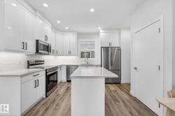 Kitchen with appliances with stainless steel finishes, a kitchen island, white cabinetry, light wood-type flooring, and recessed lighting - 