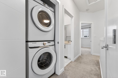 Laundry room with stacked washing machine and dryer, light tile patterned flooring, and light carpet - #5 15805 97 Ave, Edmonton, AB - Indoor Photo Showing Laundry Room