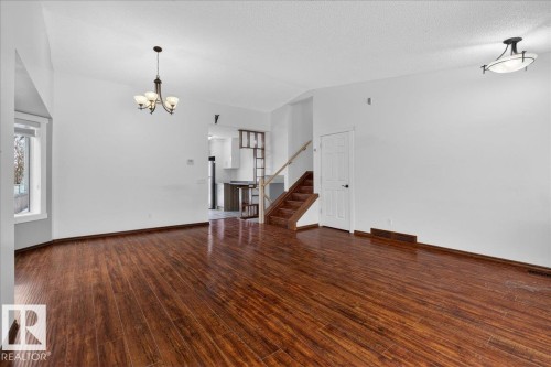 Unfurnished living room featuring dark wood-style floors, stairs, a chandelier, vaulted ceiling, and a textured ceiling - 2516 42 Street, Edmonton, AB - Indoor Photo Showing Other Room