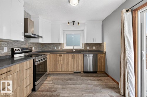 Kitchen with stainless steel appliances, dark wood-style floors, wall chimney exhaust hood, decorative backsplash, and a textured ceiling - 2516 42 Street, Edmonton, AB - Indoor Photo Showing Kitchen