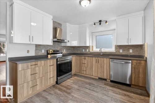 Kitchen featuring appliances with stainless steel finishes, plenty of natural light, a textured ceiling, wall chimney range hood, and dark wood-type flooring - 2516 42 Street, Edmonton, AB - Indoor Photo Showing Kitchen With Upgraded Kitchen