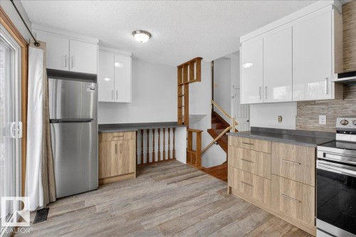 Kitchen with dark countertops, stainless steel appliances, tasteful backsplash, a textured ceiling, and light wood-style flooring - 2516 42 Street, Edmonton, AB - Indoor Photo Showing Kitchen With Upgraded Kitchen