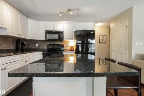 Kitchen featuring a kitchen bar, black appliances, a kitchen island, white cabinets, and dark stone counters - 2315 Lemieux Place, Edmonton, AB - Indoor Photo Showing Kitchen With Upgraded Kitchen