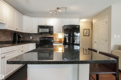 Kitchen featuring a kitchen bar, black appliances, a kitchen island, white cabinets, and dark stone counters - 