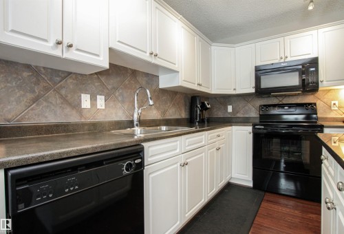 Kitchen featuring black appliances, white cabinets, dark countertops, a textured ceiling, and dark wood-style flooring - 2315 Lemieux Place, Edmonton, AB - Indoor Photo Showing Kitchen With Double Sink