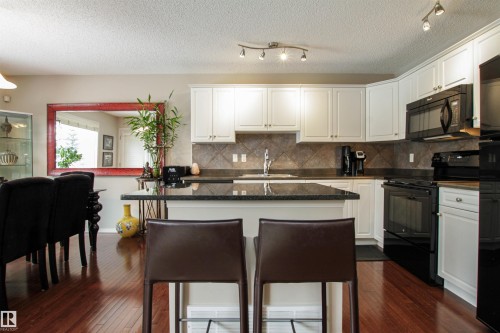 Kitchen featuring black appliances, white cabinetry, a kitchen bar, dark wood-type flooring, and a kitchen island - 2315 Lemieux Place, Edmonton, AB - Indoor Photo Showing Kitchen