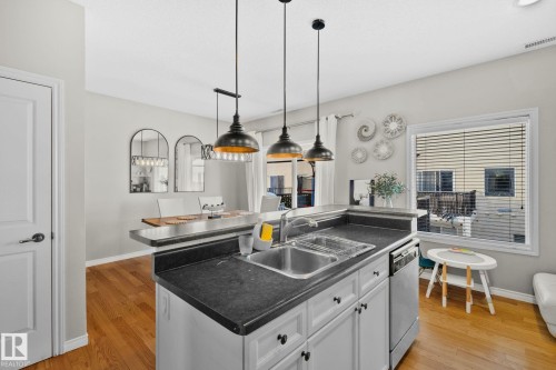 Kitchen featuring a kitchen island with sink, dark countertops, white cabinets, decorative light fixtures, and stainless steel dishwasher - 46 13825 155 Avenue, Edmonton, AB - Indoor Photo Showing Kitchen With Double Sink