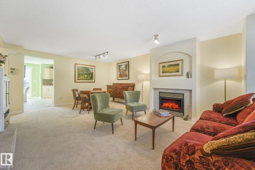 Living area with a tile fireplace, light carpet, rail lighting, and a textured ceiling - 23 4755 Terwillegar Common, Edmonton, AB - Indoor Photo Showing Living Room With Fireplace
