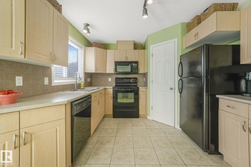 Kitchen featuring black appliances, light brown cabinets, light countertops, a textured ceiling, and light tile patterned flooring - 23 4755 Terwillegar Common, Edmonton, AB - Indoor Photo Showing Kitchen
