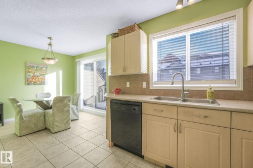 Kitchen with dishwasher, tasteful backsplash, light countertops, light brown cabinetry, and pendant lighting - 23 4755 Terwillegar Common, Edmonton, AB - Indoor Photo Showing Kitchen With Double Sink