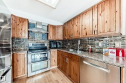 Kitchen featuring appliances with stainless steel finishes, wall chimney range hood, light wood-type flooring, brown cabinets, and decorative backsplash - 