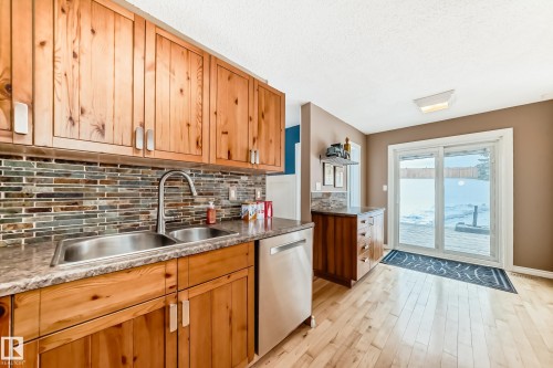 Kitchen featuring stainless steel dishwasher, brown cabinetry, decorative backsplash, light wood-style floors, and a textured ceiling - 18931 80 Avenue, Edmonton, AB - Indoor Photo Showing Kitchen With Double Sink