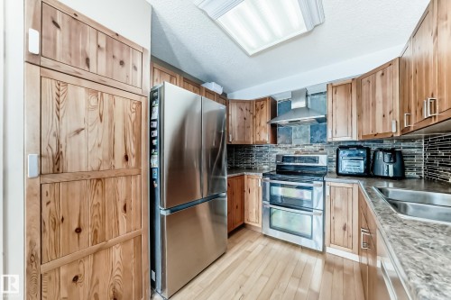 Kitchen featuring stainless steel appliances, backsplash, wall chimney exhaust hood, a textured ceiling, and light wood-type flooring - 18931 80 Avenue, Edmonton, AB - Indoor Photo Showing Kitchen With Double Sink