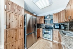 Kitchen featuring stainless steel appliances, backsplash, wall chimney exhaust hood, a textured ceiling, and light wood-type flooring - 