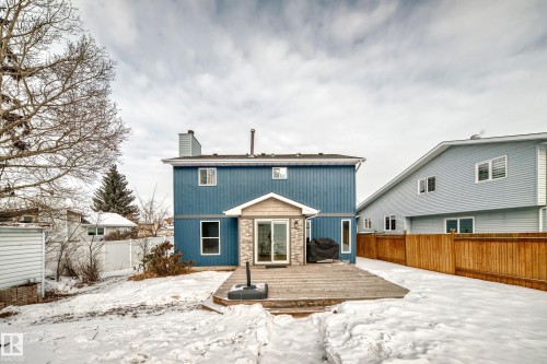 Snow covered back of property with a fenced backyard, a wooden deck, a chimney, and stone siding - 18931 80 Avenue, Edmonton, AB - Outdoor