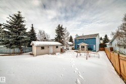 Snow covered rear of property with a fenced backyard, an outdoor structure, and a chimney - 