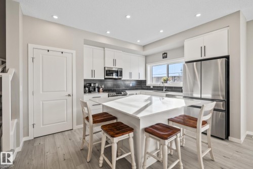 Kitchen featuring a kitchen breakfast bar, stainless steel appliances, white cabinets, a kitchen island, and backsplash - 217 Larch Crescent, Leduc, AB - Indoor Photo Showing Kitchen With Upgraded Kitchen