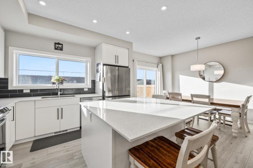 Kitchen featuring a kitchen bar, pendant lighting, white cabinets, stainless steel appliances, and light stone counters - 217 Larch Crescent, Leduc, AB - Indoor Photo Showing Kitchen With Upgraded Kitchen
