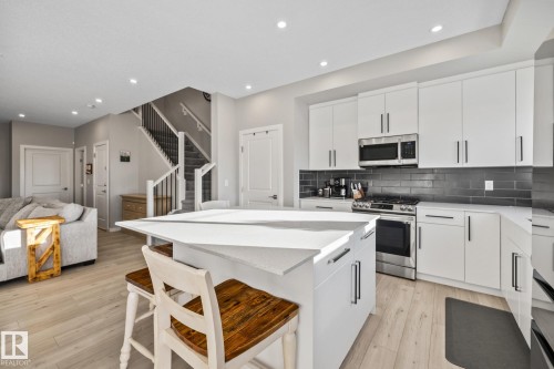 Kitchen featuring a breakfast bar area, stainless steel appliances, white cabinetry, open floor plan, and a kitchen island - 217 Larch Crescent, Leduc, AB - Indoor Photo Showing Kitchen With Upgraded Kitchen