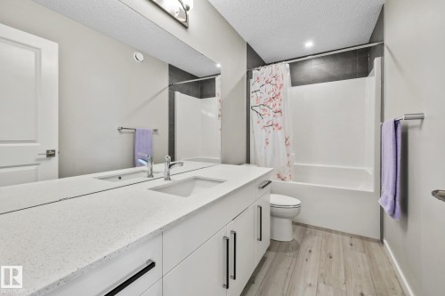 Full bathroom with a textured ceiling, vanity, shower / tub combo, and light wood-style flooring - 217 Larch Crescent, Leduc, AB - Indoor Photo Showing Bathroom