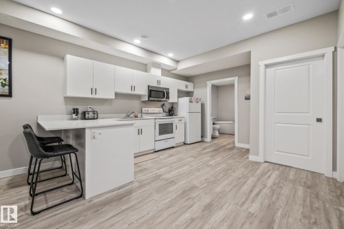 Kitchen featuring white appliances, white cabinets, a breakfast bar, a peninsula, and light wood-type flooring - 217 Larch Crescent, Leduc, AB - Indoor Photo Showing Kitchen