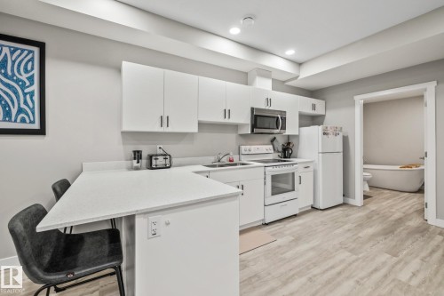 Kitchen with white appliances, a breakfast bar, white cabinetry, light wood finished floors, and a peninsula - 217 Larch Crescent, Leduc, AB - Indoor Photo Showing Kitchen