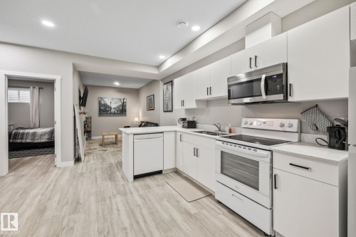 Kitchen featuring a peninsula, white appliances, light countertops, white cabinets, and light wood-type flooring - 217 Larch Crescent, Leduc, AB - Indoor Photo Showing Kitchen With Double Sink