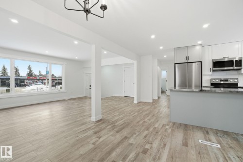 Kitchen with open floor plan, dark stone counters, stainless steel appliances, recessed lighting, and light wood finished floors - 7112 132 Avenue, Edmonton, AB - Indoor Photo Showing Kitchen With Upgraded Kitchen