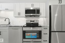 Kitchen featuring stainless steel appliances, tasteful backsplash, and white cabinets - 