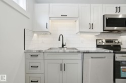 Kitchen with appliances with stainless steel finishes, white cabinetry, light stone countertops, and decorative backsplash - 