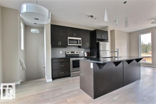 Kitchen featuring hanging light fixtures, stainless steel appliances, a breakfast bar, and an island with sink - 125 1304 Rutherford Road, Edmonton, AB - Indoor Photo Showing Kitchen With Upgraded Kitchen