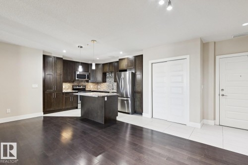 Kitchen featuring dark brown cabinets, appliances with stainless steel finishes, decorative light fixtures, a kitchen island, and recessed lighting - 208 1350 Windermere Way, Edmonton, AB - Indoor Photo Showing Kitchen With Stainless Steel Kitchen With Upgraded Kitchen