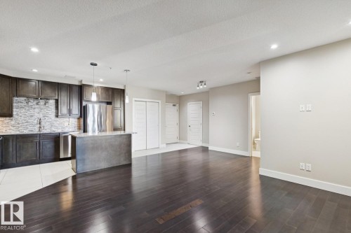 Kitchen with dark brown cabinetry, open floor plan, pendant lighting, appliances with stainless steel finishes, and a kitchen island - 208 1350 Windermere Way, Edmonton, AB - Indoor Photo Showing Kitchen With Stainless Steel Kitchen With Upgraded Kitchen